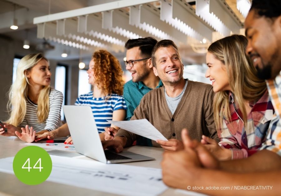 Gruppe von jungen Menschen lacht und diskutiert angeregt rund um einen Tisch – Darstellung von gelungener Motivation und Teamführung